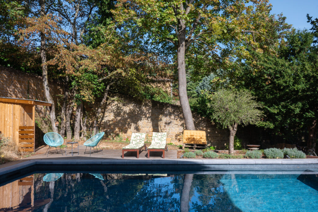 Vue du jardin arboré autour de la piscine et du mur en pierre