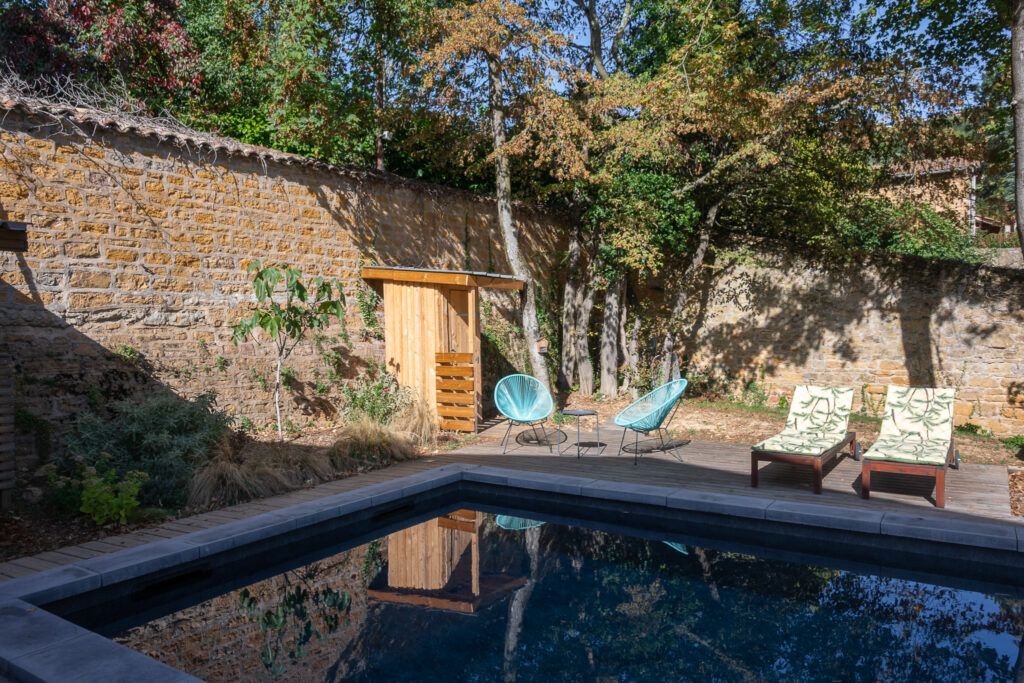 Piscine, fauteuils et petite construction en bois au pied du mur en pierre
