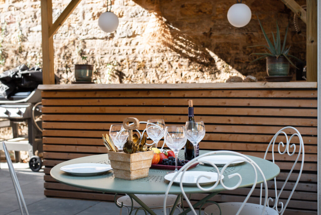 Table de jardin devant un bar extérieur en bois et un mur en pierre