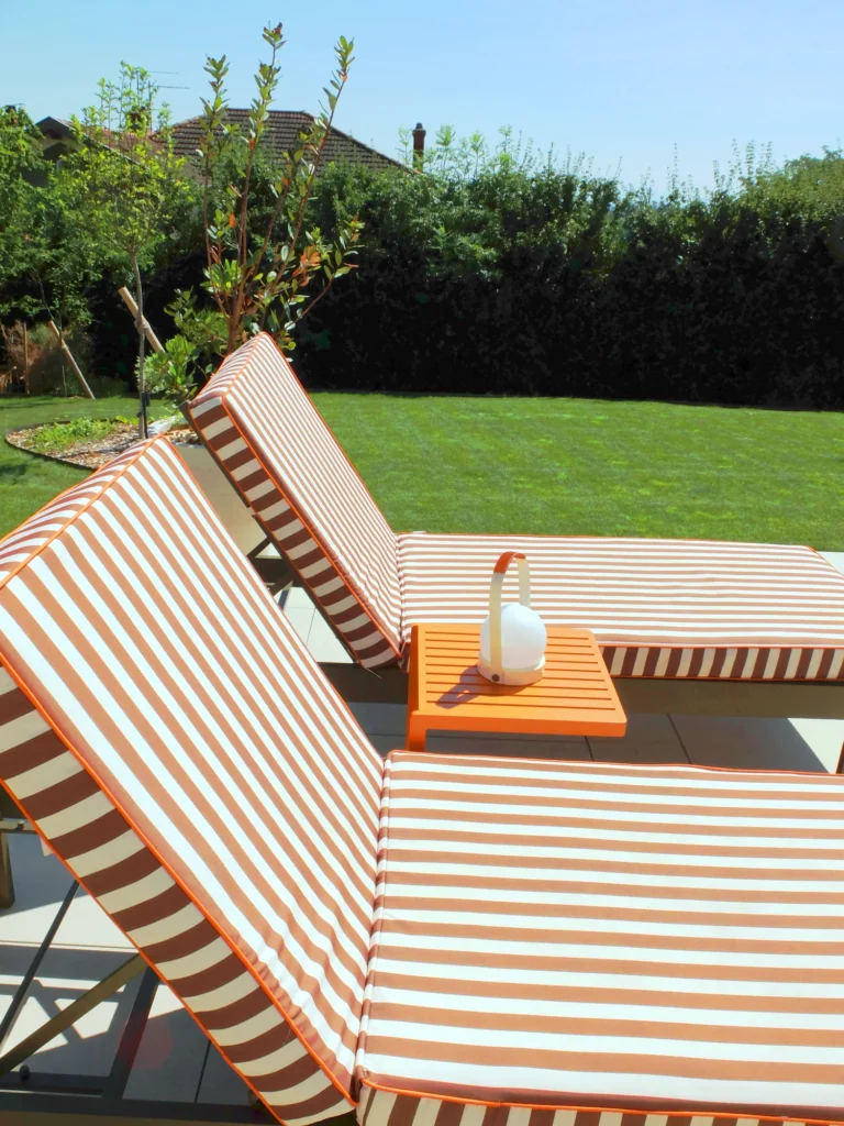 Bains de soleil en bois devant la piscine, avec pelouse et haie en arrière-plan.