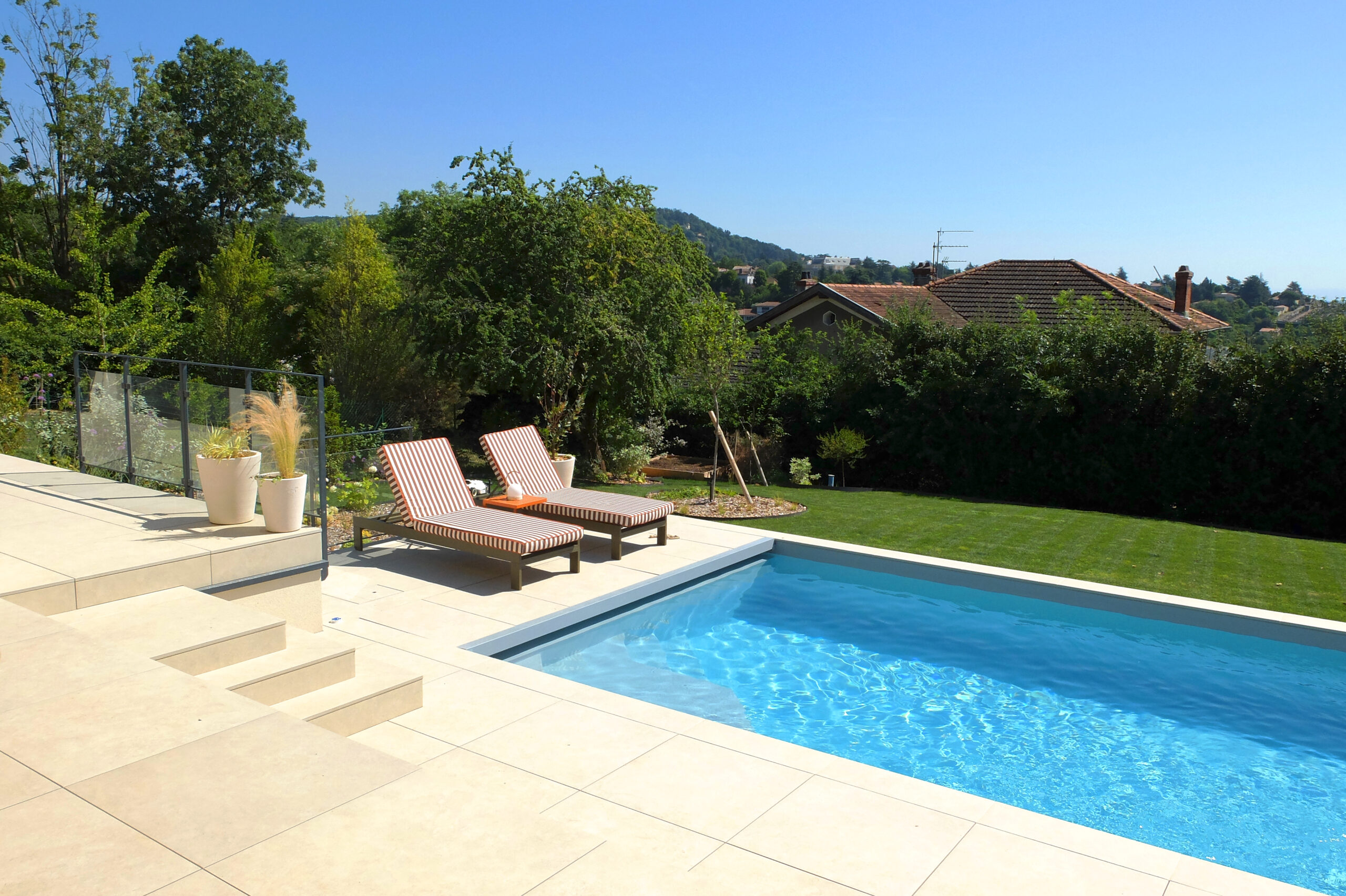 Piscine bordée d’une terrasse minérale et d’un jardin planté à Saint-Didier-au-Mont-d’Or.
