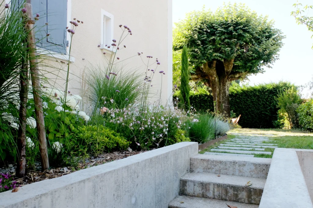 Escalier en béton et pas japonais entre la maison et les massifs du jardin Concretia à Saint-Didier-au-Mont-d’Or.